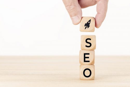 SEO or search engine optimization concept. Human hand holding a wooden block with rocket icon and SEO word. White background Copy space